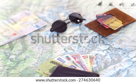 Light color composition on travel topic.  Unfolded detailed topographic map exotic Asian cash notes credit cards sunglasses passport entry stamps many