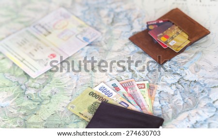 Desk of frequent traveler - angle view. The composition essential items for trip passport multiple entry stamps cash notes from different countries, wallet credit cards, detailed map on the background