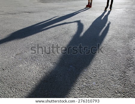 Shadows of skaters on asphalt. Paved urban road shadows of female roller skaters friends holding hands and enjoying skating together outdoor park sunlight summer day