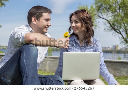 Young man and woman with flowers. Young cute male and female two people sitting in park with laptop computer casual dress code guy giving flowers to girl