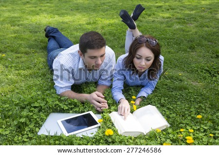 Young people working out. Man and woman casual dress code pant jeans shirt lying on grass lawn working with laptop computer tablet PC book students learning businessman out of office