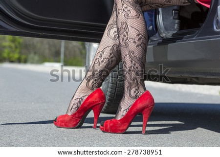 Leg of stylish female driver. Female leg dressed provocative clubbing pantyhose high heels red shoes step out of the blue car