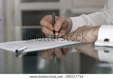 Man signs formal paper. Businessman hands working on paper document on glass office table making strong reflection with fountain pen stylish shirt with golden cuff link soft smothered background