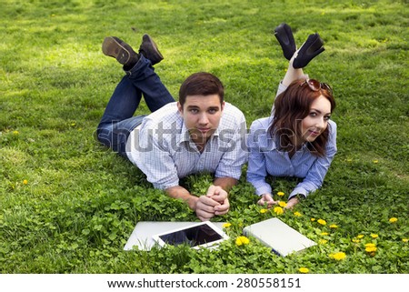 Young people working out. Man and woman casual dress code pant jeans shirt lying on grass lawn working with laptop computer tablet PC book students learning businessman out of office