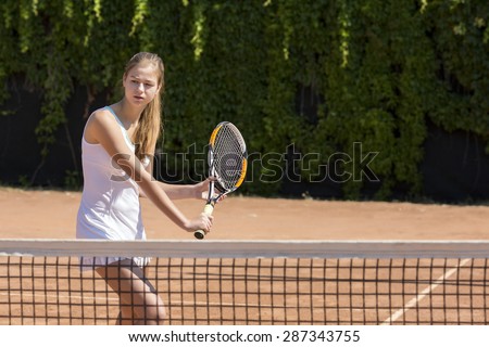 Ready to hit back.\
Young female tennis athlete swinging racket to hit coming ball white dress with miniskirt outdoor play court dark green fence background orange clay ground