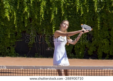 Ready to hit back.\
Young female tennis athlete swinging racket to hit coming ball white dress with miniskirt outdoor play court dark green fence background orange clay ground