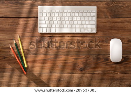 Workplace of creative person. Rough wooden desk textured brown planks with visible chocks natural pattern white modern computer keyboard mouse colorful pencils sun light coming throw venetian blinds