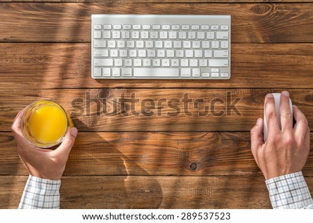 Businessman working at vintage crafted wooden desk.\
From above prospective on clean working place with keyboard mouse glass orange juice hands of person working