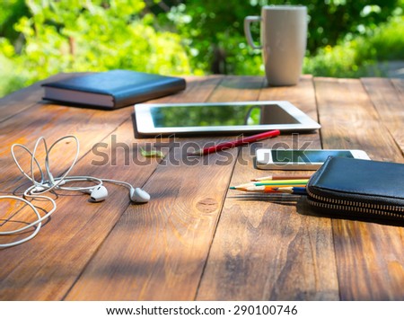 Wood desk and electronic gadgets.\
Vintage desk and selection of business items around tablet PC smart phone headphones notepad colored pencils black folder large coffee mug green flora on background