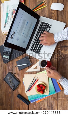 Hobby time concept vertical. Man working computer handcrafted rough wooden desk overhead top view keeping coffee mug many office supplies in creative disorder focus on plate with fresh strawberry food
