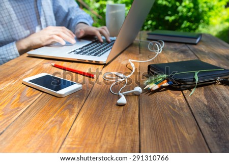 Textured wooden desk and hardworking man. Boarded handmade wooden desk with smart phone headphones pencils and grass piece male body hard working on his electronic mail on laptop