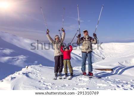 Winter sport family. Family of three people - parents and little daughter - on winter mountains background happy laughing faces victory raised hands with poles