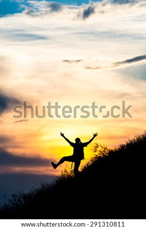 Happy female silhouette making funny dance. Woman making dancing moves on steep grassy hill with gorgeous sunset sky and cloudscape on background