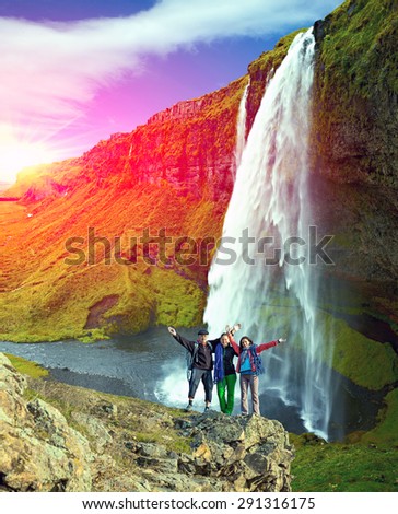 Embracing people on waterfall background. Family of three people together on hike in Iceland stays together large terrific large waterfall green hills and shining sun on background