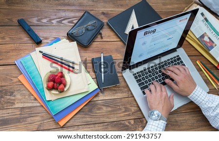 Journalist working on his new article.\
Overhead view of man typing on keyboard laptop located vintage natural wooden desk with many items in creative messy disorder