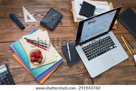 Vacation entertainment concept. \
Handcrafted countryside style wooden desk items in creative disorder laptop computer internet page on screen color pencils booklets plate strawberry