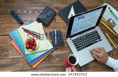 Journalist working on his new article.\
Overhead view of man typing on keyboard laptop located vintage natural wooden desk with many items in creative mess