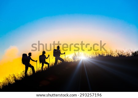 People meeting sunrise team building session. Group of people silhouettes walking toward mountain summit with backpacks and hiking trekking gear meeting uprising sun sunbeams and blue sky background