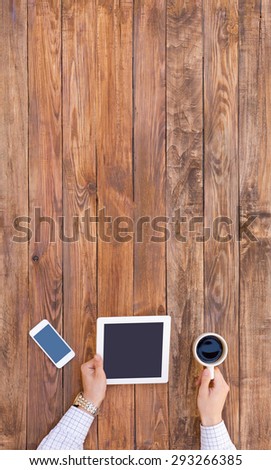 Business dressed Human arms holding tablet PC and white coffee mug and large copy space on natural hardwood textured background