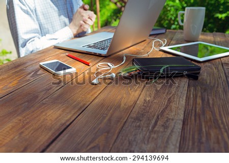 Businessman working at laptop out of office rubbing his hands gesture beginning new task green flora sunlight background handcrafted brown wood desk electronic devices and office accessories around