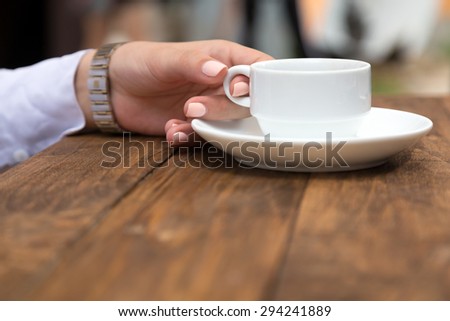 Female hand holding white coffee mug at grunge wood desk