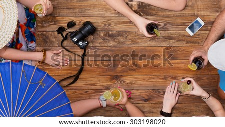 Beach party scene. Summer vacation style dressed group young people relaxing with cocktails at cafe terrace bar vintage rough wooden desk directly from above