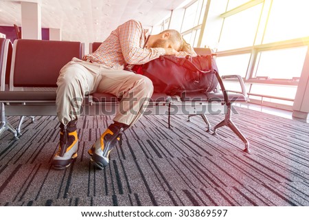 Canceled flight. \
Man sleeping on his travel luggage inside airport terminal with back light bright sun coming throw window