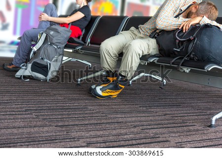 Bodies of people waiting airport terminal. Man and woman sitting at chairs waiting lounge airport building sleep on backpack informal sport dress code pants shirt luggage colorful interior background