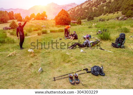 Hikers break on grassy lawn. Group tourists doing break male observing mountain landscape females lean on heavy loaded backpacks with tons of climbing gear leader guide aged mature packing his bag sun