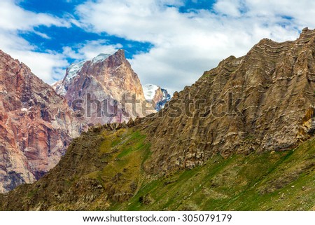 Mountain landscape with unusual perspective.\
Bright color layers of highland formation with grassy ridge on foreground and red orange rocky wall on background with glaciers and snow on top of peak