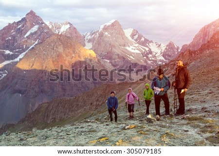 People on mountain pathway.\
Multinational group of hikers staying on mountain pass with high peaks and rising sun on background