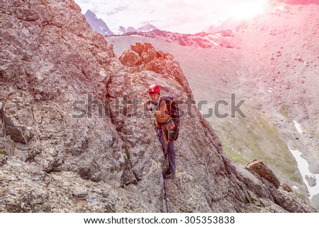 Person climbs mountain Female mountain climber traversing bright orange red rock moving towards point of shoot color mountain range and rising sky on background