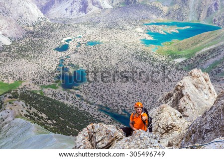 Mountain guide pointing. Mature mountain guide leading his team pointing with his hand best way to go hanging over deep abyss with vivid blue lakes on blurred background