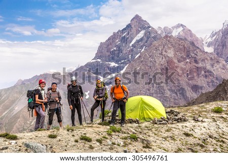 Alpine climbers team and camp. Group of five people men and women staying along green camping tent on majestic mountain landscape of deserted Asian area
