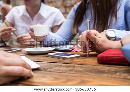 Group of young people at cafe table Conceptual image of people hands around vintage natural wood desk drinking coffee using pen, telephones and other gadgets at open space terrace