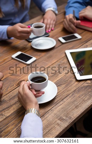 Coffee break.\
Business people drinking coffee at wooden plank table modern electronic gadgets dropped around