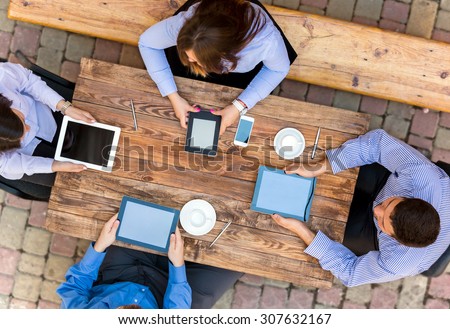 Business people with Digital Devices at cafe Table.\
Group of Business People Using Digital Devices Sitting at Wood Desk From Above