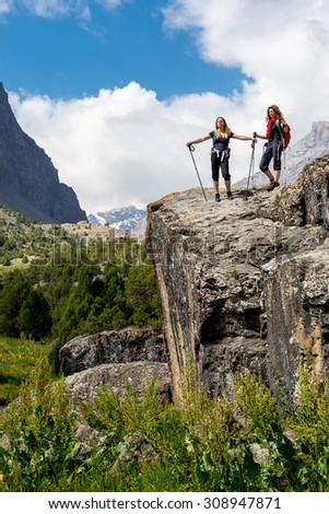 Outdoor life.\
People walking on top of stone rock with trekking poles and backpacks silhouettes on clouds and sky background mountain landscape young women