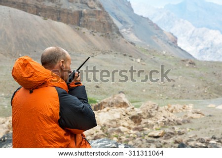 Man Talking on Radio.\
Mountain Rescue Officer Holding Radio Walkies Talkie and Severe Mountain Landscape Background