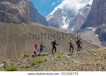 Diverse Team Walking on Rocky Ridge.\
Grassy Ridge and Group of People Walking with Hiking Gear Severe High Mountain Landscape Background Blue Sky White Clouds