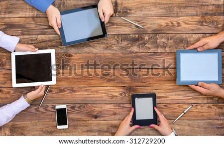 Male and Female Arms with Digital Gadgets.\
Natural Rough Wooden Plank Desk and Four People Holding Working Electronic Devices Tablet PC Book Notepad Smart Telephone
