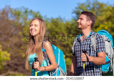 Excited Travelers Young Man and Woman Traveling Outdoor Expressing Fun and Pleasure with Backpacks Walking Poles Sticks and Casual Sporty Style Clothing
