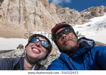 Joyful Alpine Climbers Self Portrait\
Faces of Smiling Man and Woman Sport Style Clothing Protection Helmets Sunglasses High Altitude Mountain Landscape with Rock and Snow on Background