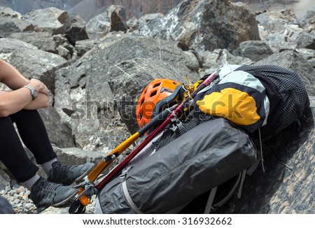 Alpine Backpack with Climbing Gear Attached Backpack with Climbing Gear Attached Outside Sport Orange Helmet Ice Axe and Hummer Mat and Tent Legs of Woman on Left Side Rocky Terrain on Background