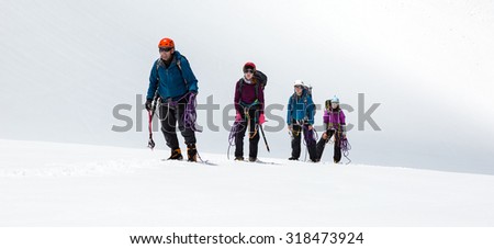 Group of Climbers Approaching to Summit\
Four People Staying on Mountain High Altitude Snowfield Sporty Clothing and Safety Climbing Gear Mature Male Guide and Young Female Athletes