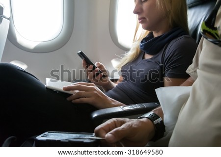 Air Flight Passenger Sitting in Aircraft\
Casual Clothing Woman in Plane Seat Browsing Her Smart Phone and Holding Documents for Immigration Formalities Hand of Man on Foreground Focus on Female Hands