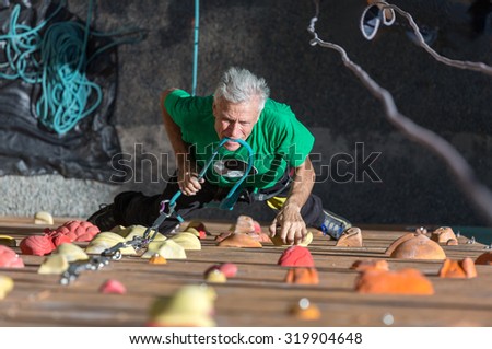 Mature Athlete Fixing Rope into Belaying Device\
Aged Male Climber Moving Up on Outdoor Climbing Wall on Veterans Extreme Sport Competitions