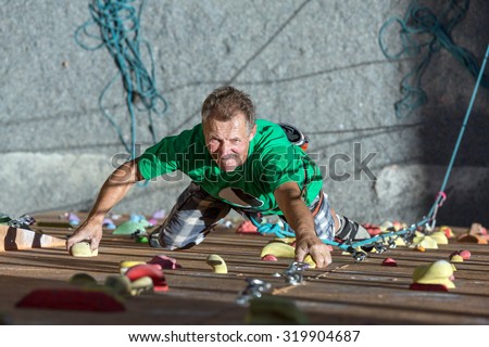 Smiling Mature Man on Extreme Climbing Wall\
Portrait of Handsome Adult Male Climber Moving Up on Sport Training Course in Outdoor Climb Gym\
Using Rope Belaying Gear with Positive Inspired Face Emotion