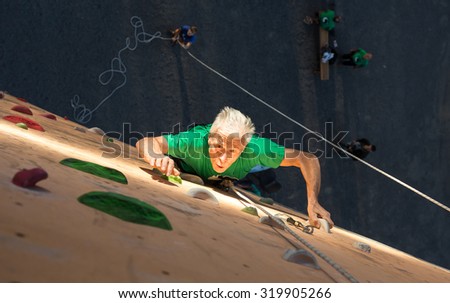 Aged Person Practicing Extreme Sport\
Elderly Male Climber Makes Hard Move on Outdoor Climbing Wall Sport Competitions Very Emotional Face Highlighted with Spotlight of Illumination