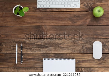 Brown Wooden Desk with Stationery Electronics Flora and Food\
Natural Wood Background Small Green Plant and Apple Computer Mouse and Keyboard Black and White Pens Blank Notepad Top View